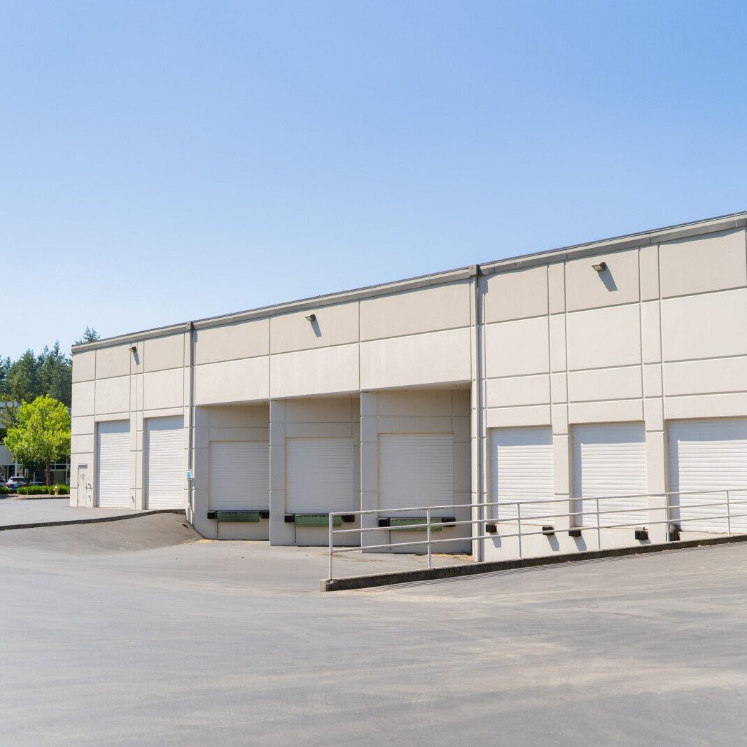 Industrial warehouse building with multiple white roll-up doors and a loading ramp under a clear blue sky, expertly maintained by a leading South Sound property management company.