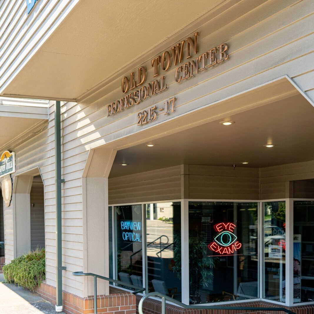 Exterior view of Old Town Professional Center, featuring a neon "Eye Exams" sign and an optician’s sign—an ideal site managed with expert South Sound commercial property management services.