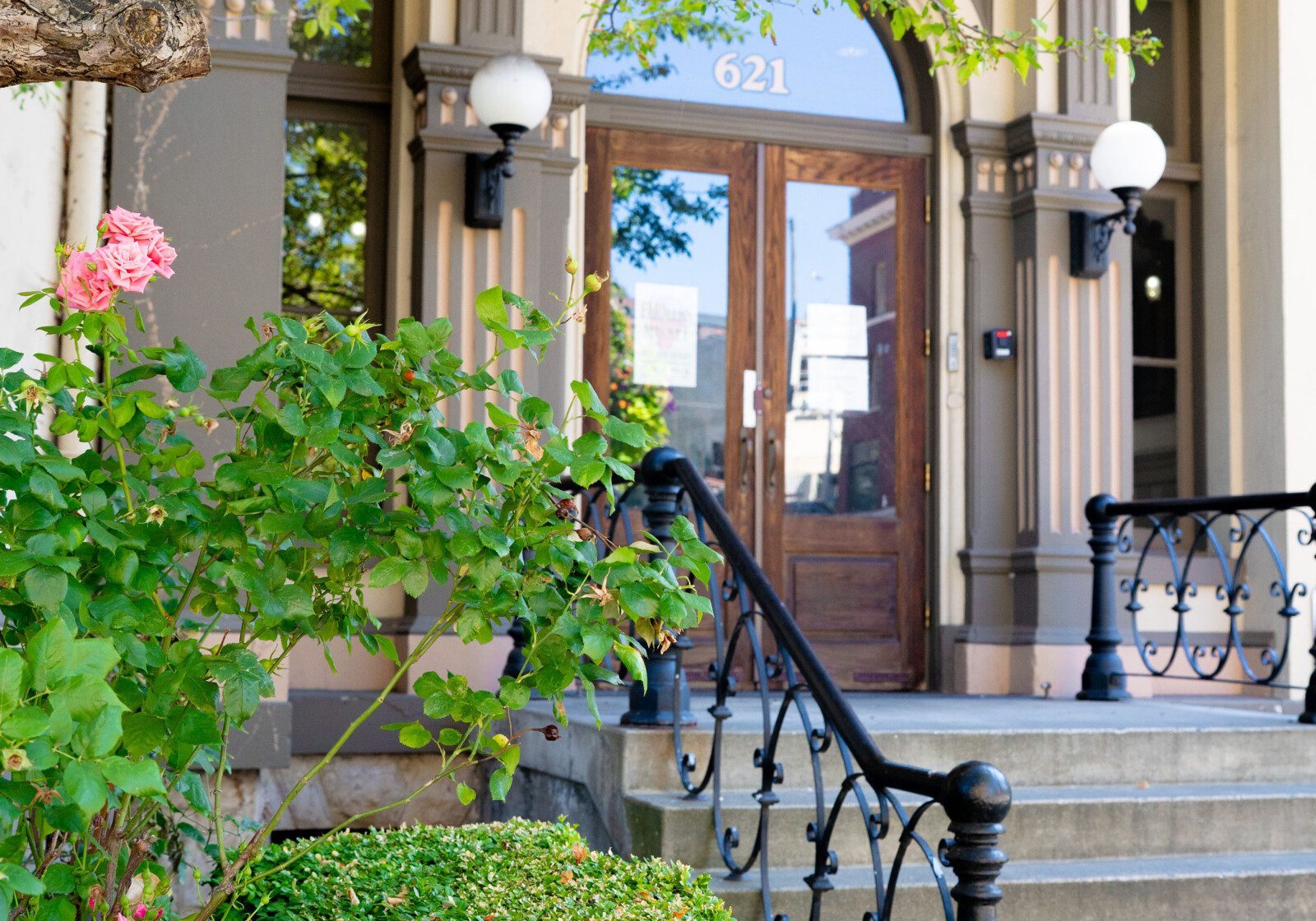 Stone steps with a black metal railing lead to a wooden door at 621, framed by arched windows, with trimmed bushes and pink flowers in the foreground—a prime example of South Sound commercial property management excellence.