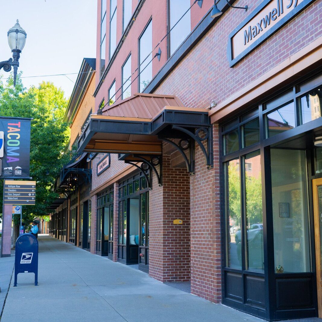 Storefronts along a brick building in downtown Tacoma, Washington, with a streetlamp, USPS mailbox, and an Interstate 5 sign on the sidewalk—an inviting scene for South Sound commercial property management opportunities.