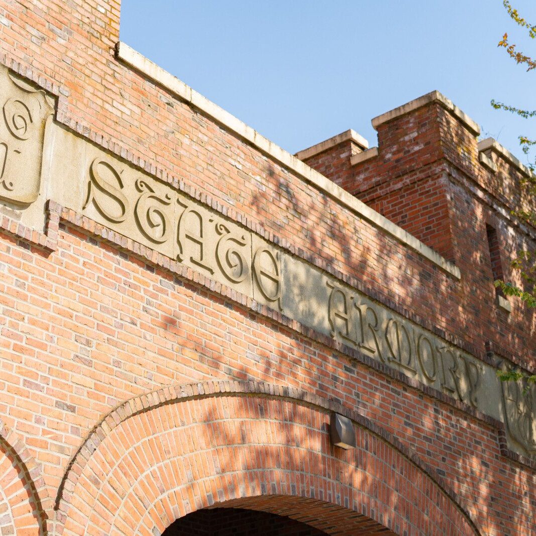A red brick building with an arched entrance, displaying "State Armory" carved in stone above the doorway, stands as a prime example of historic charm often managed by a South Sound property management company.